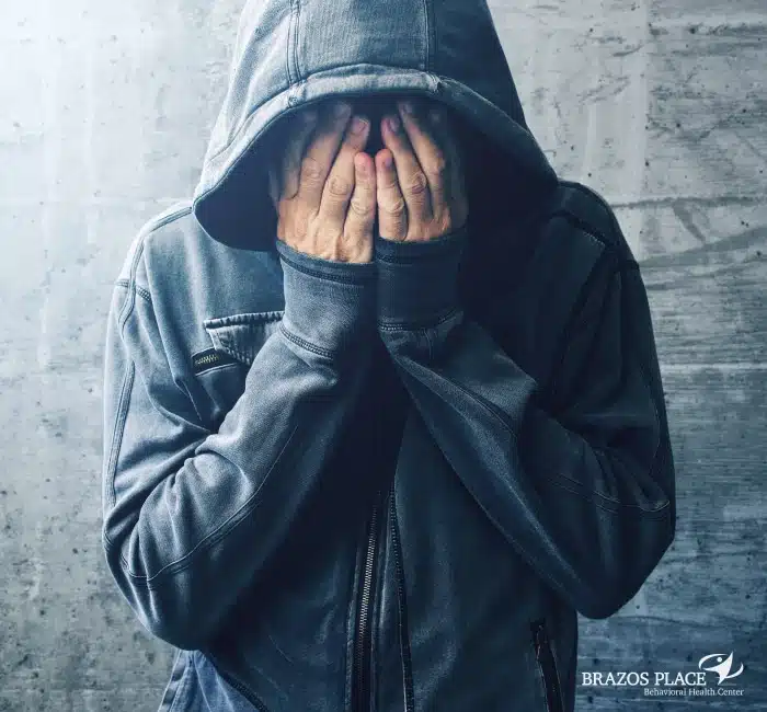 A man in hoody covering his face with his hands